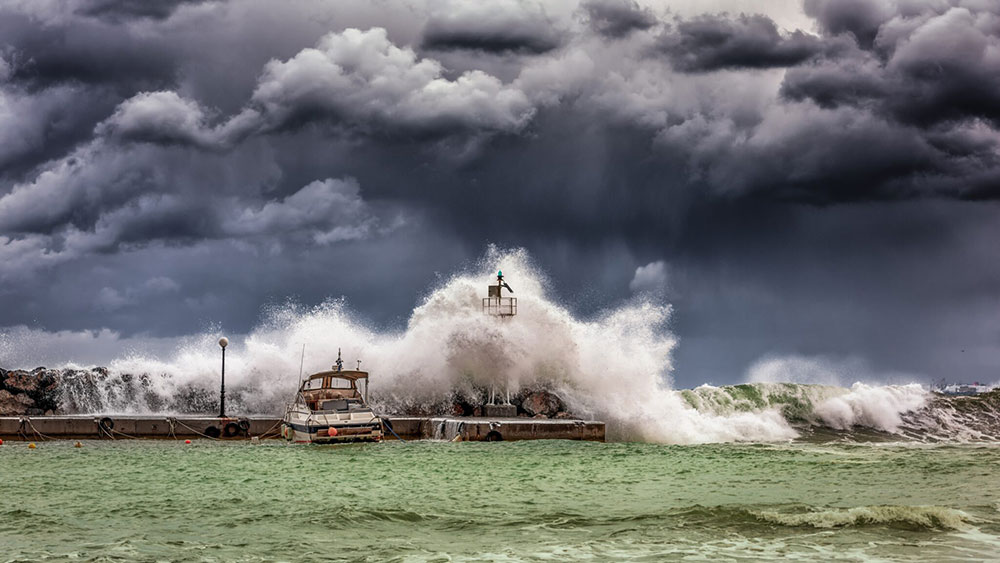 Wave on stormy seas crashing into boat and lighthouse