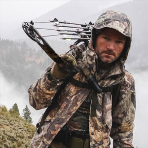 Hunting guide with compound bow hiking in the mountains