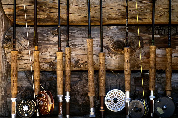 Custom fly rods and reels lined up in a row in front of a wood wall.